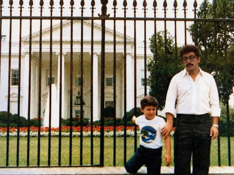 Man and child standing outside White House gates, man wearing white shirt and child in graphic t-shirt